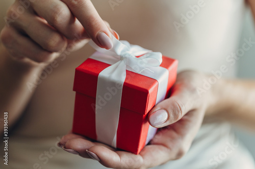 Close-up of female hands holding a small gift wrapped with a satin ribbon © Nana_studio
