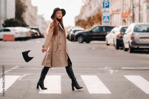 Stylish young woman in a beige coat in a black hat on a city street. Women's street fashion. Autumn clothing.Urban style