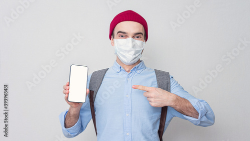 Joyful guy in a medical mask points at the phone, portrait, mock up, 16:9 photo