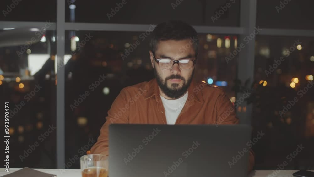 Arc shot of young businessman sitting at desk in dark office and working on laptop in the evening Arc shot of young businessman sitting at desk in dark office and working on laptop in the evening