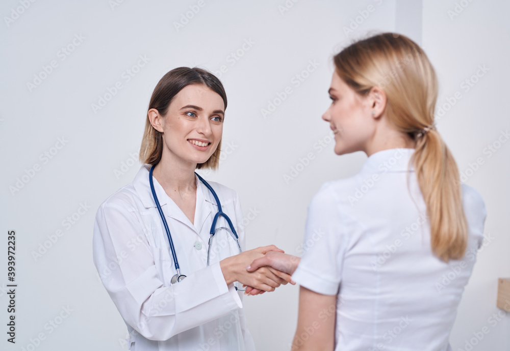 Professional doctor woman shakes hand of a female patient on a light background Professional doctor woman shakes hand of a female patient on a light background