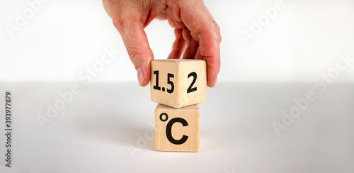 Symbol for limiting global warming. Male hand turns a cube and changes the expression '2 C' to '1.5 C', or vice versa. Concept. Beautiful white background, copy space. photo