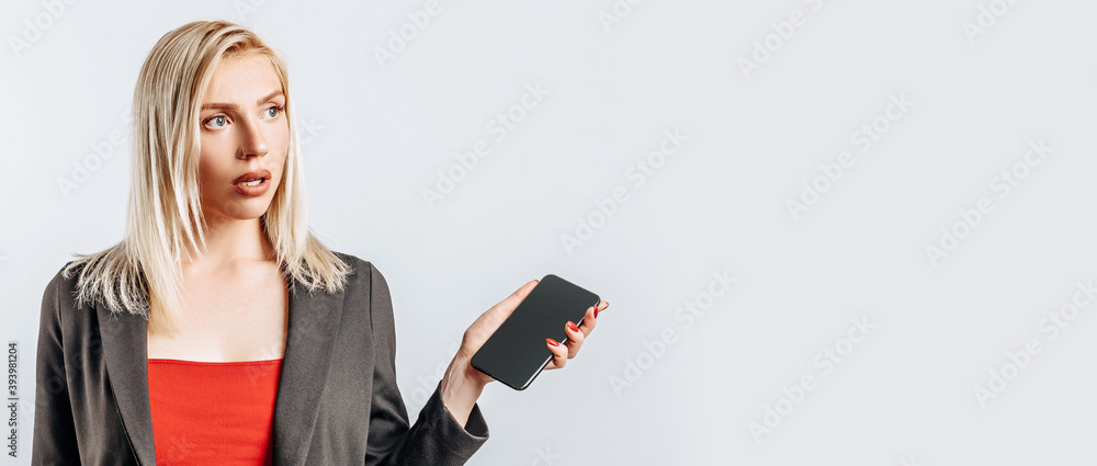 Beautiful young girl unhappy and holding phone on gray isolated background Beautiful young girl unhappy and holding phone on gray isolated background