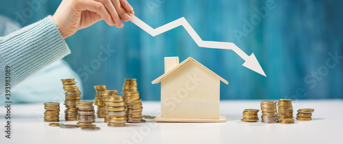 Woman holds an arrow down over model of the house and stack of coins. photo