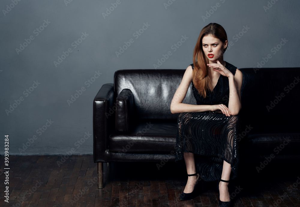 Elegant woman in evening black dress on a leather sofa indoors Elegant woman in evening black dress on a leather sofa indoors
