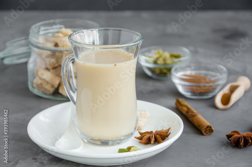 Hot tea with milk, cinnamon, cardamom, anise and other spices, Indian masala tea in a glass on a dark background. copy space.