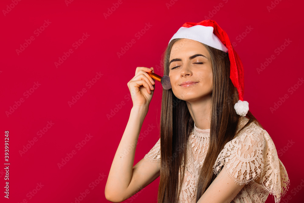 Girrl in a Santa hat powder cheeks, closed eyes, isolated on a pink with space. Girrl in a Santa hat powder cheeks, closed eyes, isolated on a pink with space.
