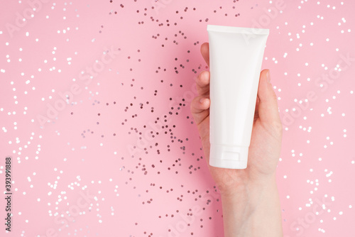 Skin care concept. Close up top above overhead view photo of female hand holding showing cream bottle over pastel pink desk background with shiny dots