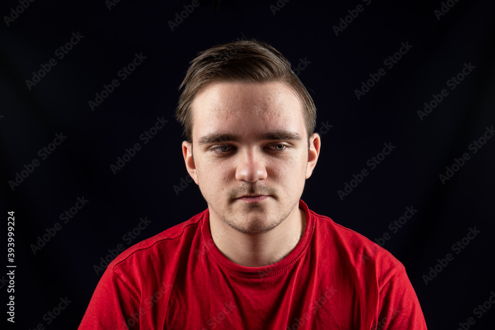 Young man in casual t-shirt standing against isolated dark background