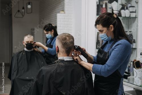 Barber shops, hair salons shutting down, second lockdown. Hairdresser in face mask peeling and combing male client in hair salon. Hairdresser and man client are wearing protective face masks.