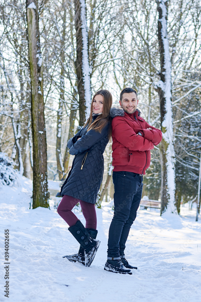 Young couple in love, enjoying winter weather outside in park forest. Brunette man in red jacket and woman in black, standing back to back,smiling. Christmas and new year holidays joy. Romantic date. Young couple in love, enjoying winter weather outside in park forest. Brunette man in red jacket and woman in black, standing back to back,smiling. Christmas and new year holidays joy. Romantic date.