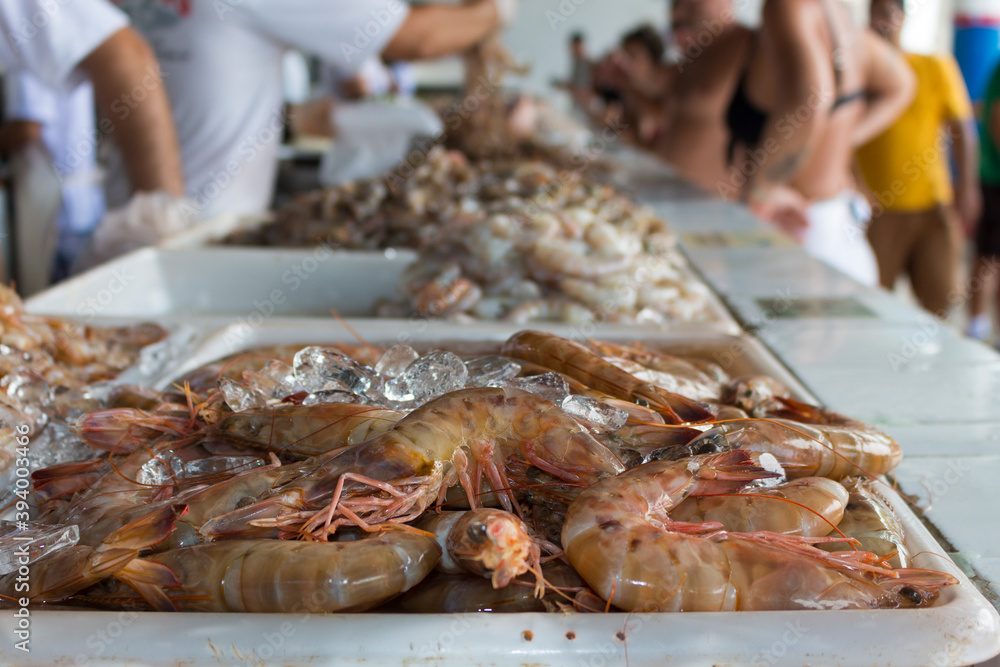 Fresh shrimp on tray preserved on ice. Coastal fish and fish market. Blurred people in the background buying seafood.