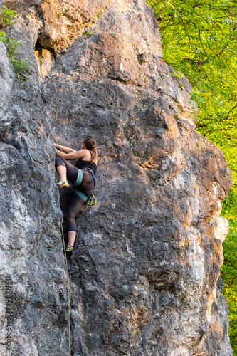 happy beautiful caucasian woman with long brown hair rock climbing, flexing her muscles on a sunny day in the mountains, strongly holding on to cliffs. Healthy outdoor sports and activities in nature