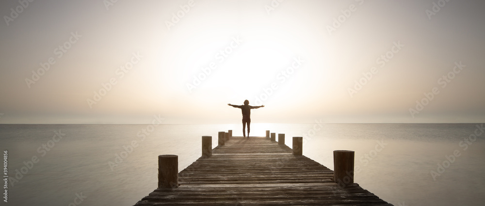 Person stands with open arms on the pier at sunrise. Powerful mediations,  relaxation, recharge your batteries and enjoy life. Stock Photo | Adobe  Stock