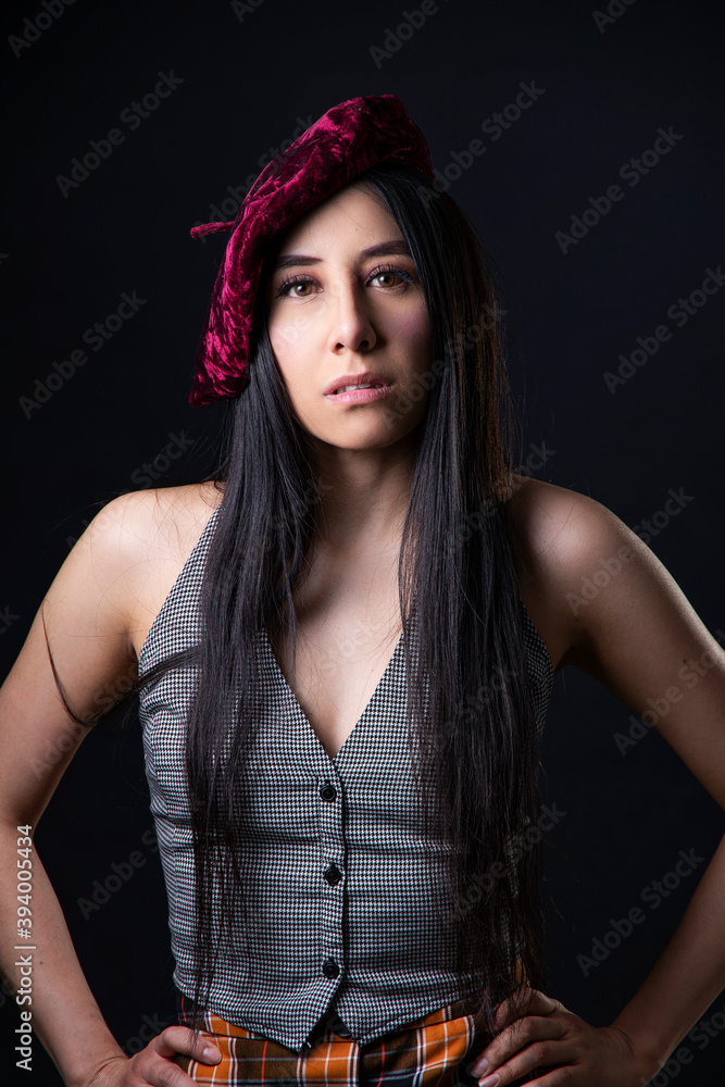 Fototapeta premium Fashion studio portrait of a young latin woman with long black hair wearing a red beret in a dark background