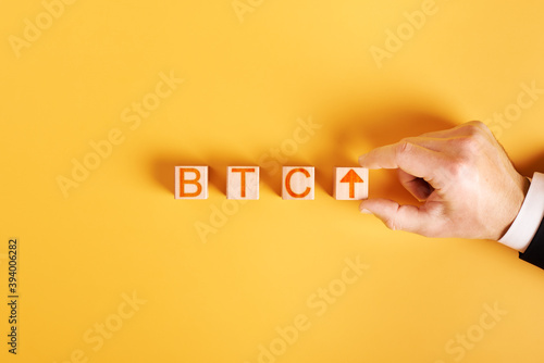 btc up. businessman puts wooden cubes in the inscription btc with an arrow up on an orange background