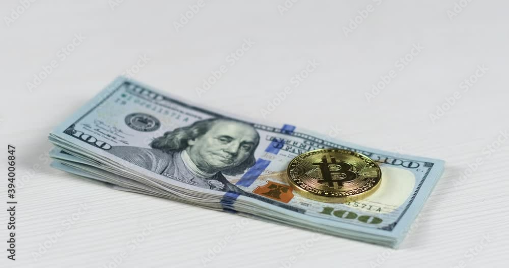 Close up, of a man placing a bitcoin coin with his hand on a stack of one hundred dollar bills. Bitcoin's weight against the dollar. Close up, of a man placing a bitcoin coin with his hand on a stack of one hundred dollar bills. Bitcoin's weight against the dollar.
