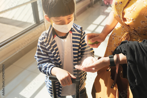 Travle safe during Covid-19 pandemic concept. Portrait of an adorable asian boy hand sanitizer with 70% alocohol by his mother while travelling to prevent coronavirus. New normal, New lifestyle  photo