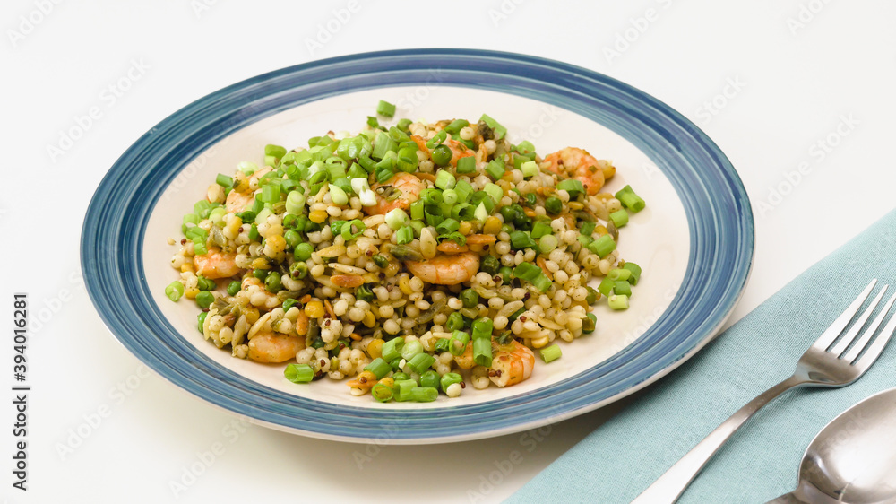 Pan-fried shrimp and blend of couscous, orzo, garbanzo beans, and red quinoa served with green peas and green onion close up on a plate on white background Pan-fried shrimp and blend of couscous, orzo, garbanzo beans, and red quinoa served with green peas and green onion close up on a plate on white background