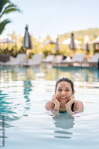 Asian woman in swimsuit smiling in swimming pool, active summer vacation concept.