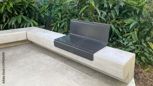 Pre cast concrete park corner bench seat with lush garden bed in the background. Ismay reserve metal and concrete street furniture. Homebush, Sydney photo