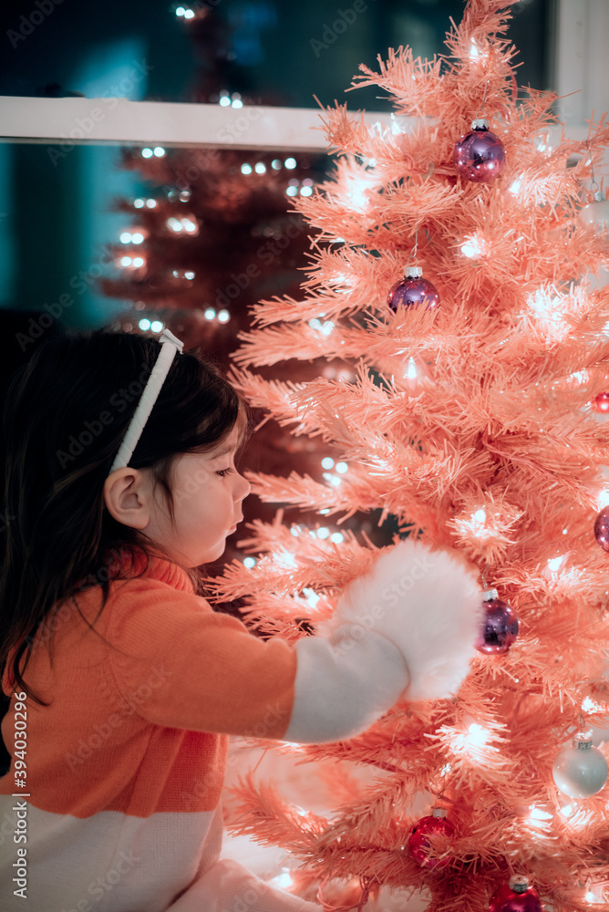 Child decorating a pink Christmas tree with twinkle lights at