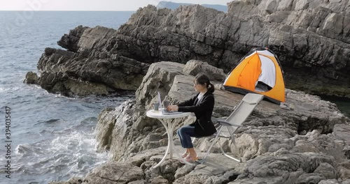 Female Business woman sitting on the rock above the sea and typing on laptop. Freelancer working from the beach. Working from distance concept. 