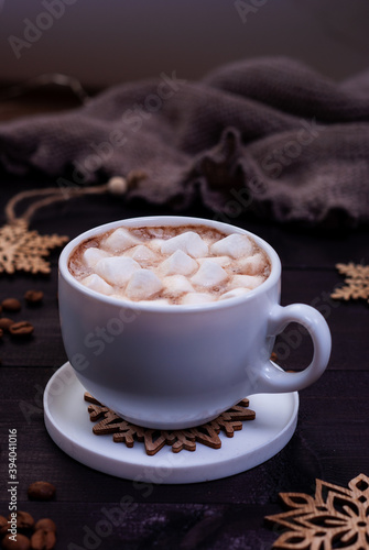 Cup of coffee with marshmallows and wooden snowflakes on dark wooden table. Winter concept, dark mood photo.