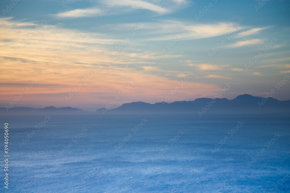 The Indian ocean and a mountain range, shrouded in mist, with silhouettes against the sky. Cape Point in South Africa.