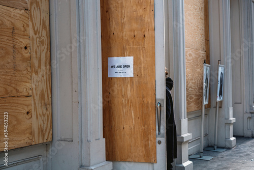 We Are Open sign greats customer entering a NYC retailer small business that has boarded up their storefront with plywood over Broadway building in fear of looting damage during the BLM protests.
