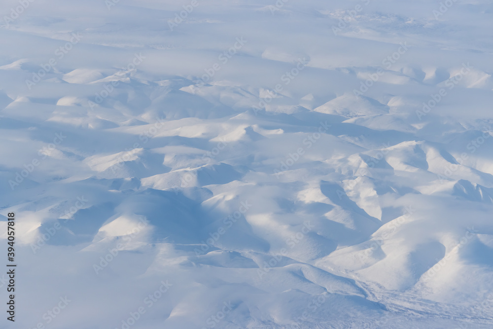 Fototapeta premium Aerial view of snow-capped mountains and clouds. Winter snowy mountain landscape. Icheghem Range, Kolyma Mountains. Koryak Okrug (Koryakia), Kamchatka Krai, Siberia, Far East Russia. Great background.