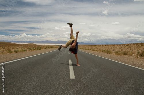 B boy. Recreational. Young caucasian man handstand and twirl in the asphalt desert road.