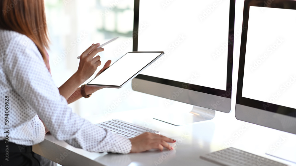 Cropped shot of two businesspeople are consulting on their project with digital tablet and multiple screen computer in modern office. Cropped shot of two businesspeople are consulting on their project with digital tablet and multiple screen computer in modern office.