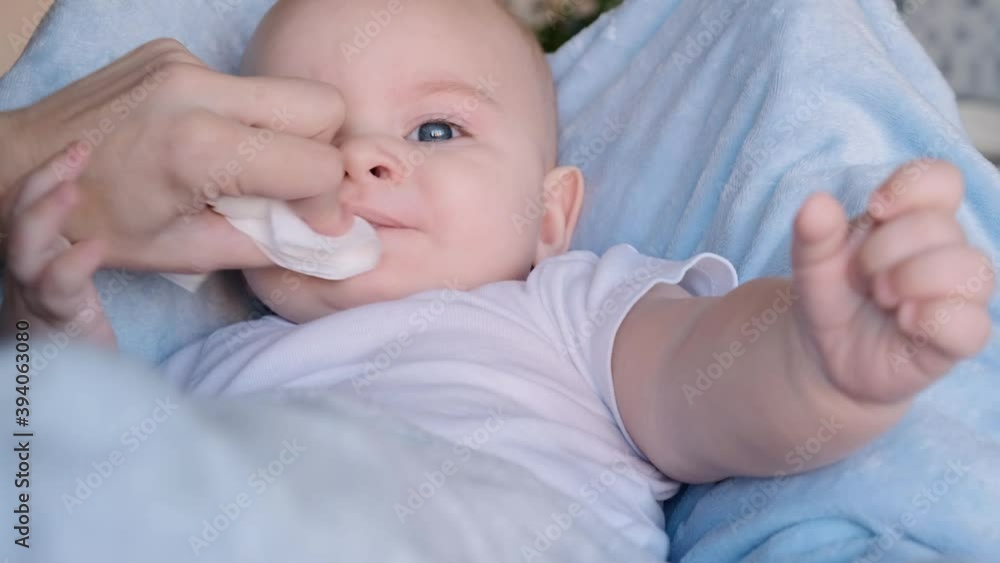 Mother wiping son's mouth after eating. Cute little 6 month old baby boy eating with funny grimace. Mother wiping son's mouth after eating. Cute little 6 month old baby boy eating with funny grimace.