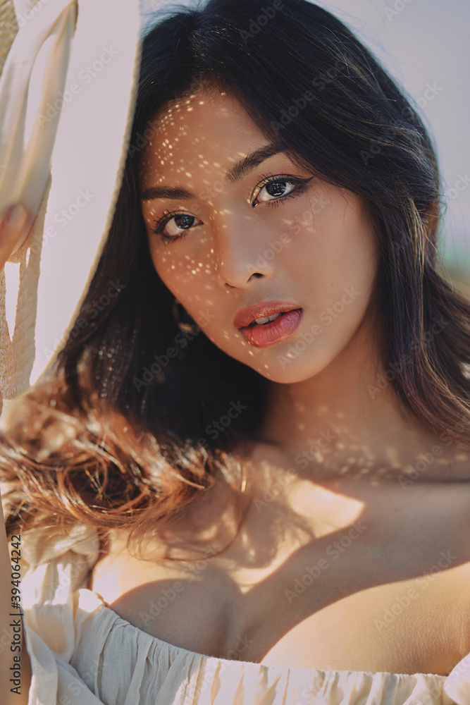 Lifestyle fashion portrait of stylish young asian woman with straw hat posing outdoor . Wearing straw hat and beige outfit .Summer bright colors.