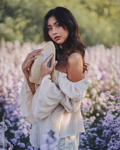 Obraz na płótnie Lifestyle fashion portrait of stylish young asian woman with straw hat posing at the flowers field . Wearing straw hat and beige outfit .Summer bright colors. w salonie