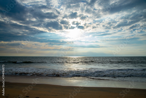 Blue ocean beach sunset with blue cloudy sky and sun rays.