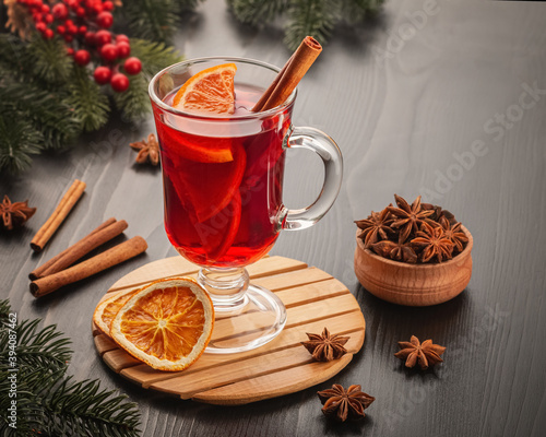 Mulled wine with several orange slices and cinnamon on a wooden table. Nearby are spruce branches with red berries and anise stars.