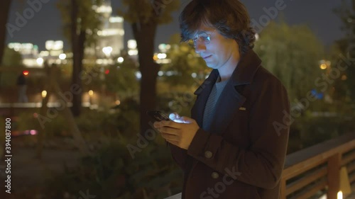 Smiling hipster typing in smartphone in the park near playground at the evening. Steadicam shot