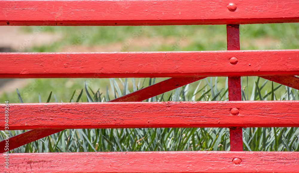 A green field seen through the parallel slats in a red painted wood fence image in horizontal format A green field seen through the parallel slats in a red painted wood fence image in horizontal format