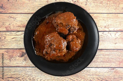 Tableau sur toile Ration of bullfighting oxtail stewed in black plate, on wooden table