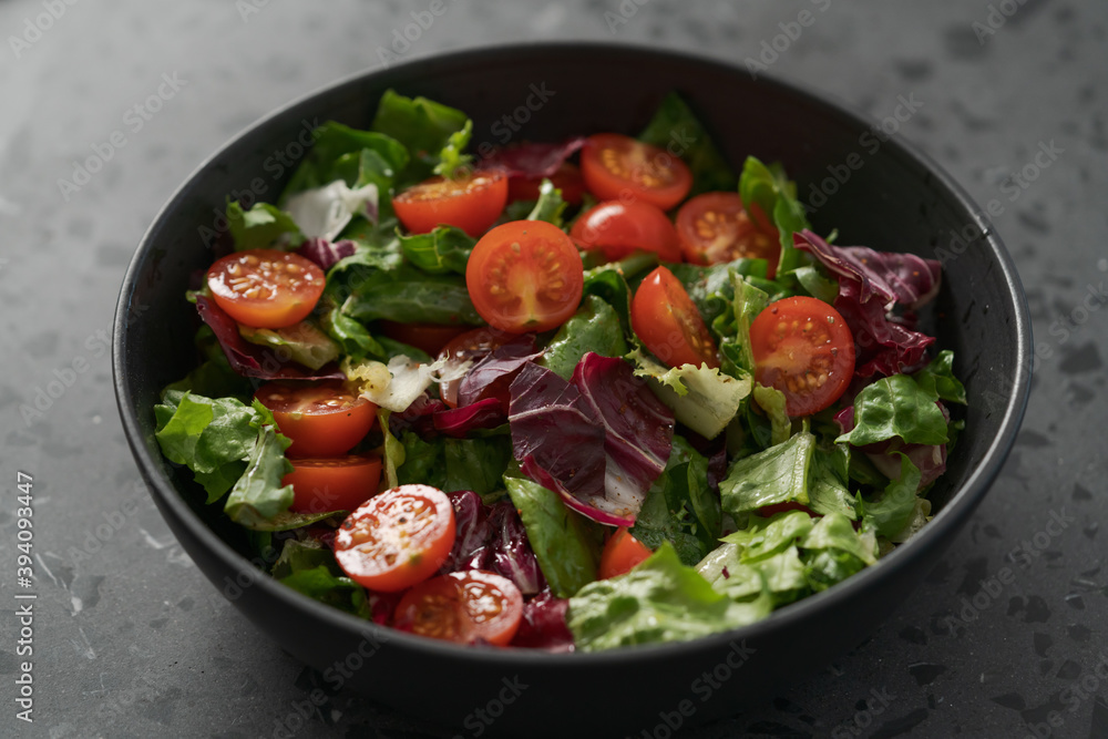 Salad with green and purple leaves and cherry tomatoes in black bowl
