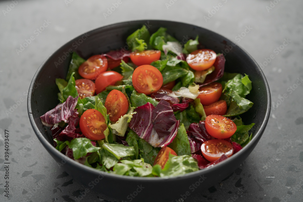 Salad with green and purple leaves and cherry tomatoes in black bowl Salad with green and purple leaves and cherry tomatoes in black bowl