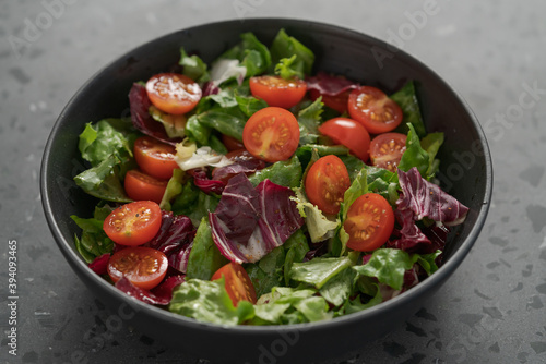 Salad with green and purple leaves and cherry tomatoes in black bowl