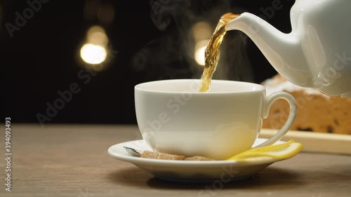 Close-up cup of tea with lemon and sugar. Hot tea pouring into a cup on black background. Steam rises above the cup. Macro shot with slide or move camera, dolly
