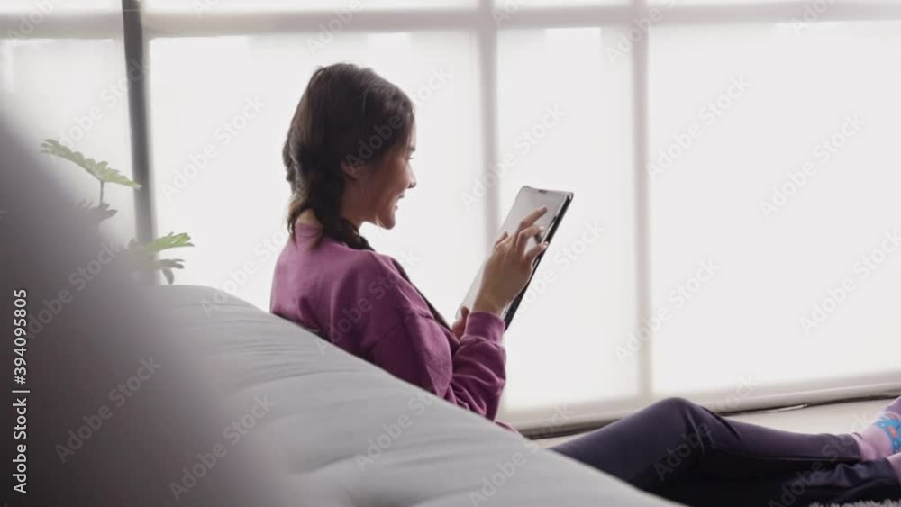 Happy young asian woman relaxing at home sit on sofa holding digital tablet enjoying surfing internet study work shopping online using social media apps or playing game on device at home. Happy young asian woman relaxing at home sit on sofa holding digital tablet enjoying surfing internet study work shopping online using social media apps or playing game on device at home.
