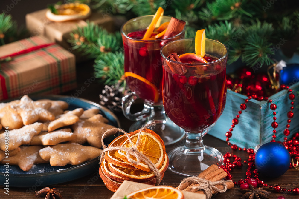 Hot wine drink with spices and fruits in a tall glass and gingerbread cookies, oranges and branches of a Christmas tree on the background. Christmas mulled wine or punch.