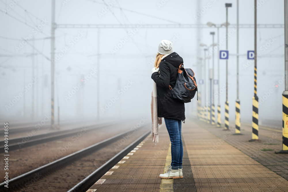 Woman waiting at railroad station for train. Foggy atmospheric mood in city