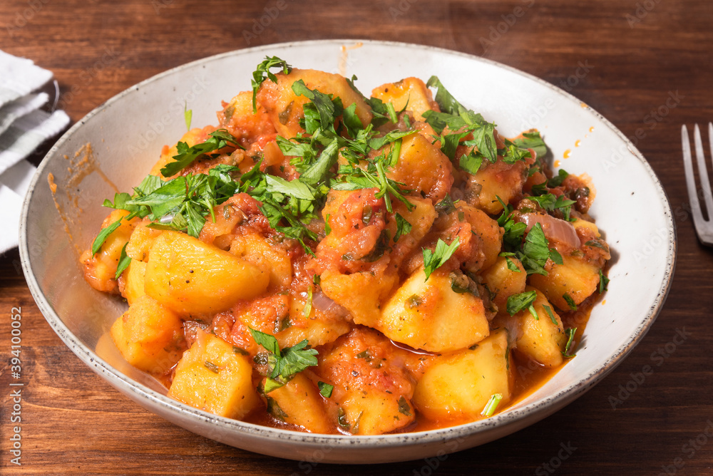 Greek vegetable stew of potatoes and vegetables in tomato sauce in a plate on a wooden table, top view, close-up Greek vegetable stew of potatoes and vegetables in tomato sauce in a plate on a wooden table, top view, close-up