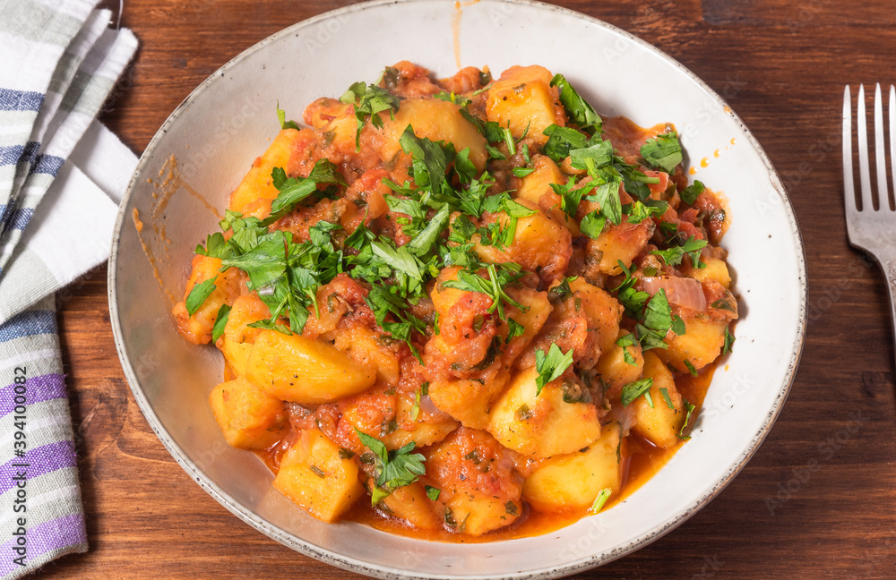Greek vegetable stew of potatoes and vegetables in tomato sauce in a plate on a wooden table, top view, close-up Greek vegetable stew of potatoes and vegetables in tomato sauce in a plate on a wooden table, top view, close-up